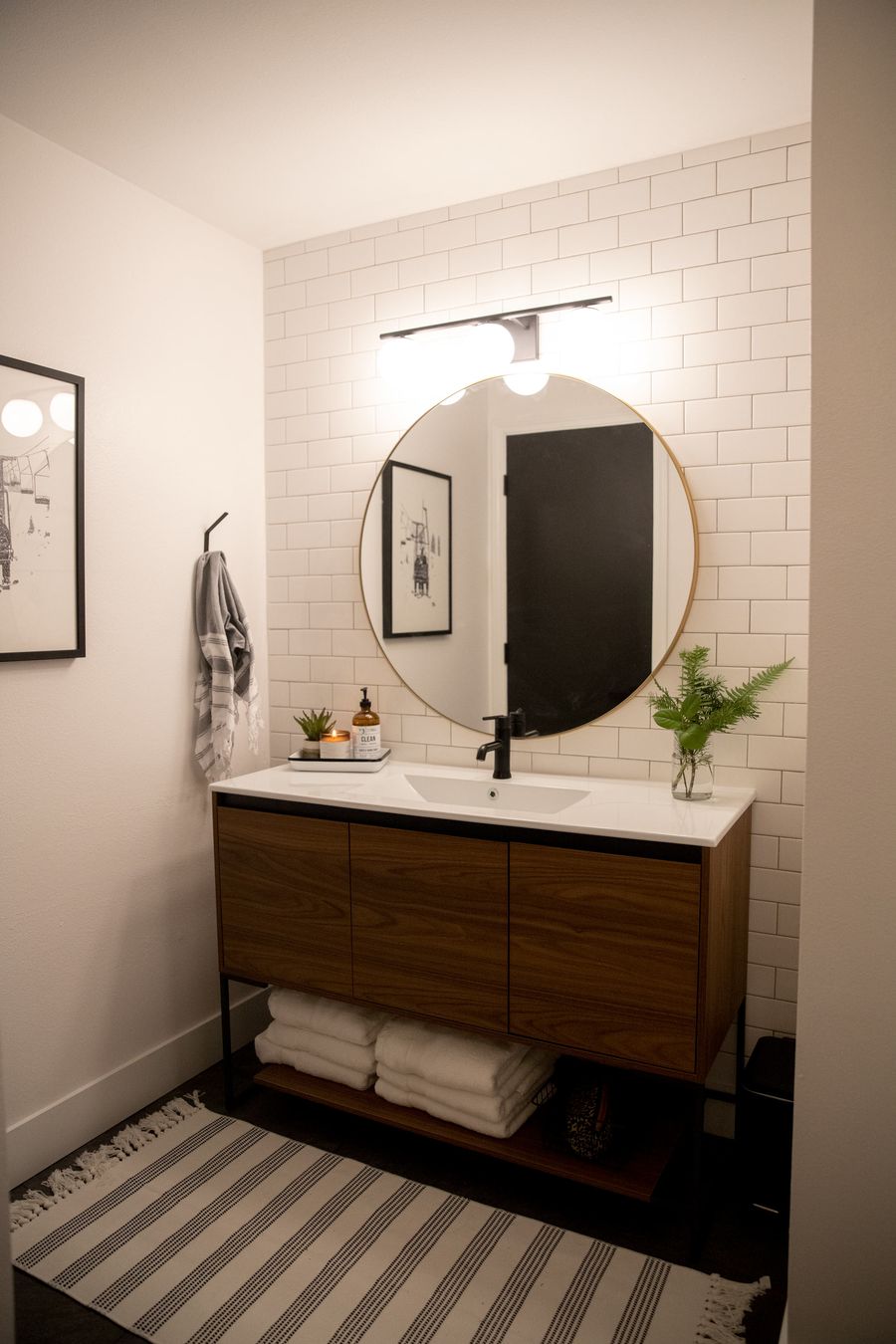 Bathroom with a walnut vanity, round mirror and white subway tile